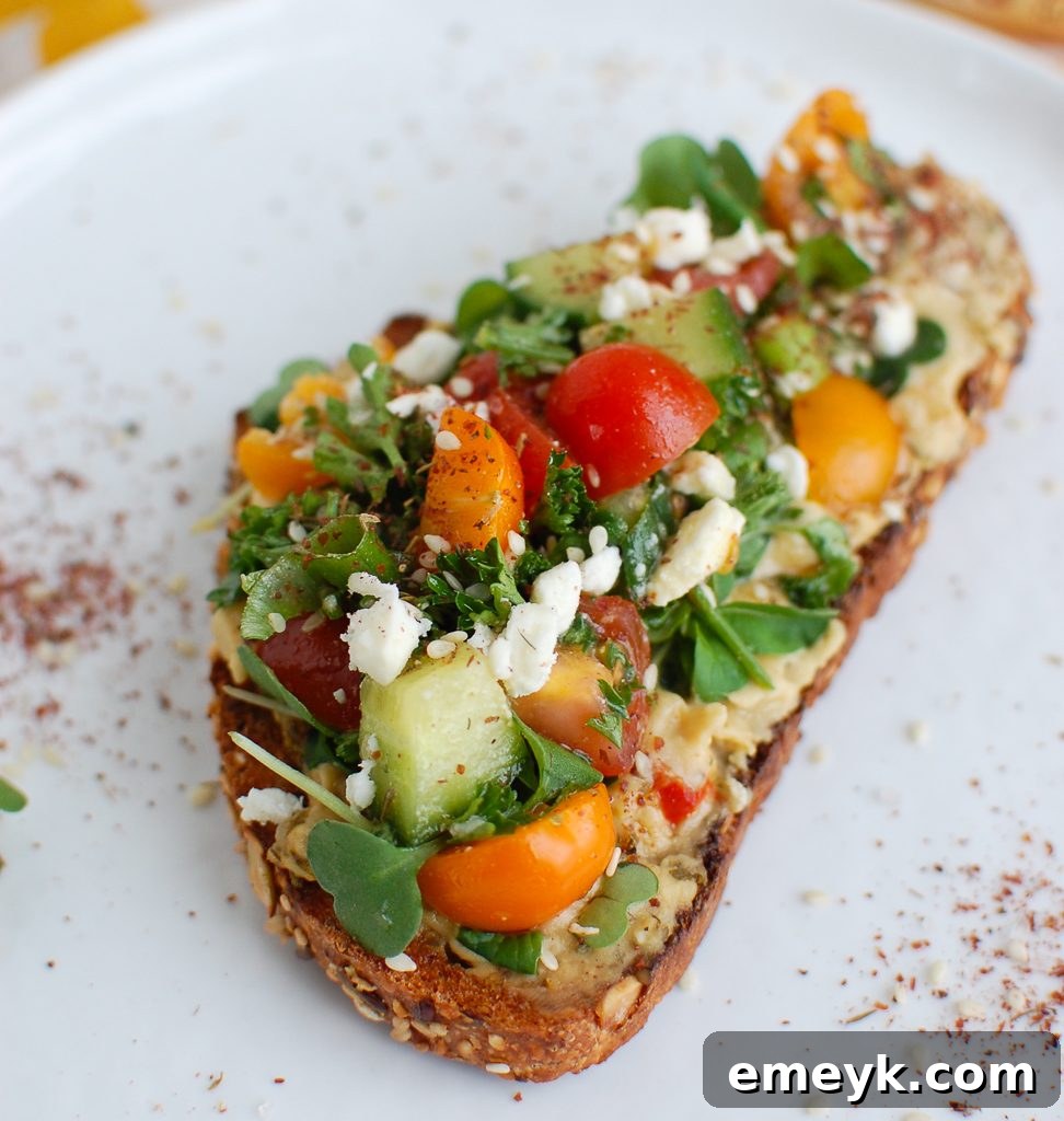 A single piece of Mediterranean Hummus Toast with Za'atar, showcasing the vibrant toppings on a white plate.