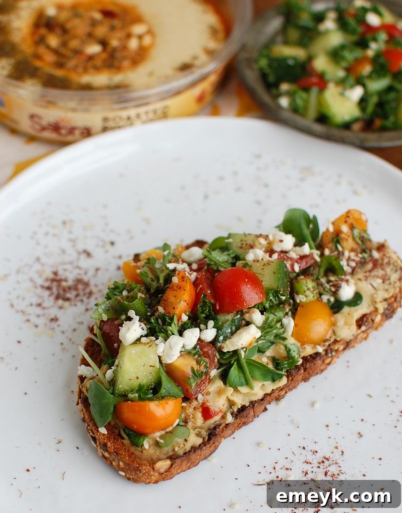 Fresh vegetables like tomatoes, cucumbers, and herbs arranged around Mediterranean Hummus Toast with Za'atar, highlighting the fresh ingredients.