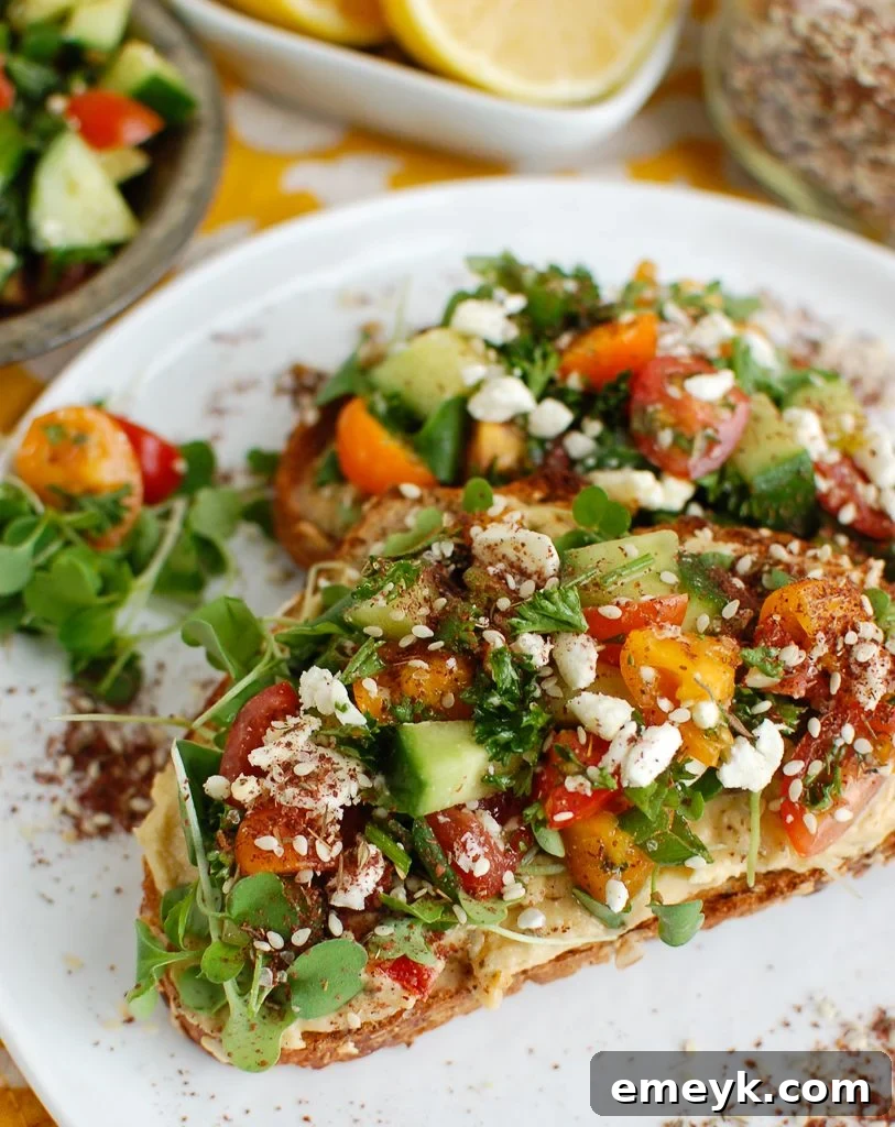 Plant-Powered Plates: 20 Recipes for Peak Energy and Vitality 7 Mediterranean Hummus Toast with Za'atar on White Plate, topped with fresh tomatoes, cucumbers, and feta.
