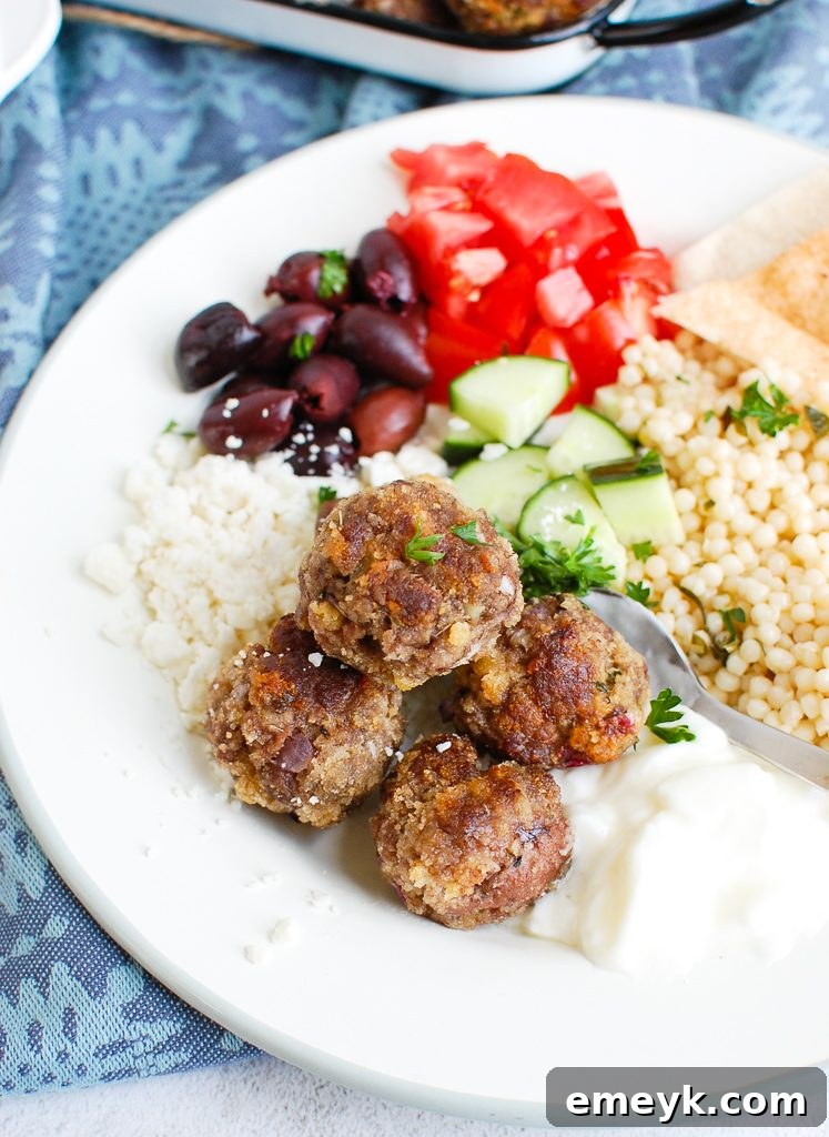Delicious Greek Meatballs served on a white plate, garnished with fresh herbs and lemon wedges.