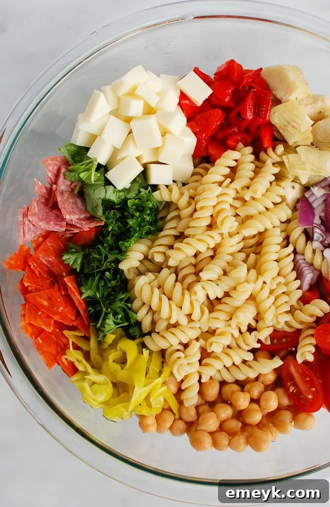 Individual ingredients for Italian Pasta Salad laid out on a wooden cutting board, including fresh herbs, cheeses, vegetables, and cured meats.