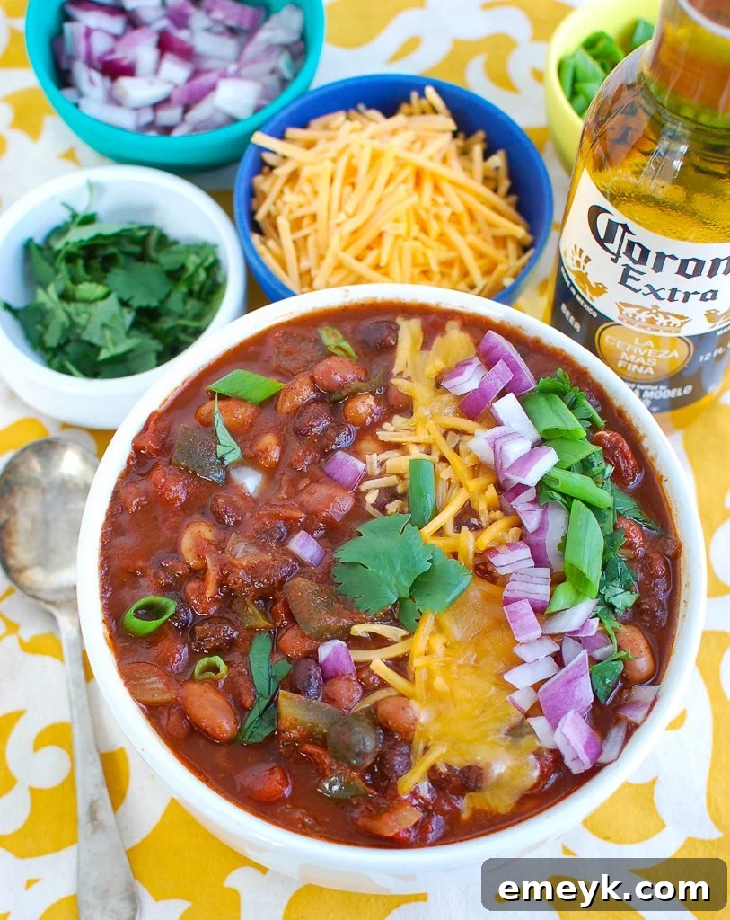 Overhead view of a white bowl filled with Slow Cooker Vegetarian Chili, garnished with avocado slices, green onions, and cilantro