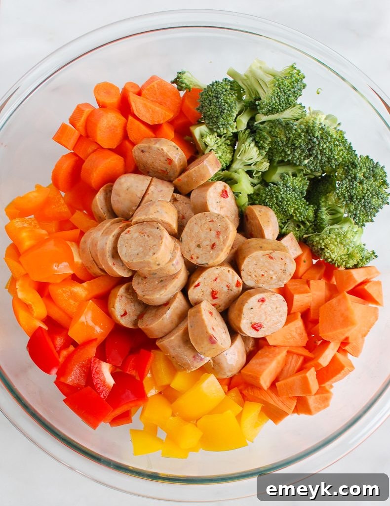 One-Pan Roasted Chicken Sausage and Vegetables 5 A vibrant display of fresh ingredients for Sheet Pan Chicken Sausage and Vegetables, including sweet potatoes, broccoli, bell peppers, carrots, and chicken sausage.