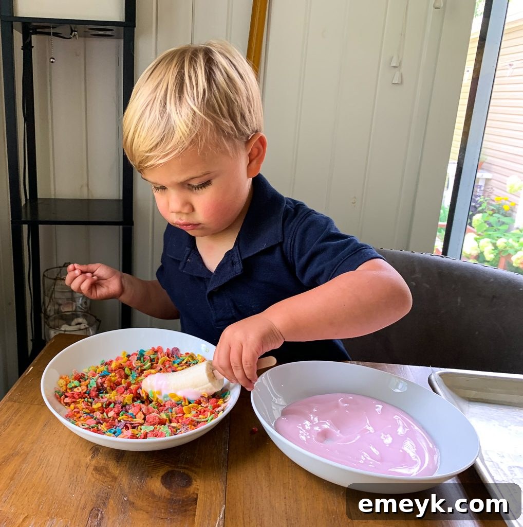 Kids hands excitedly making Banana Crunch Popsicles with colorful cereal