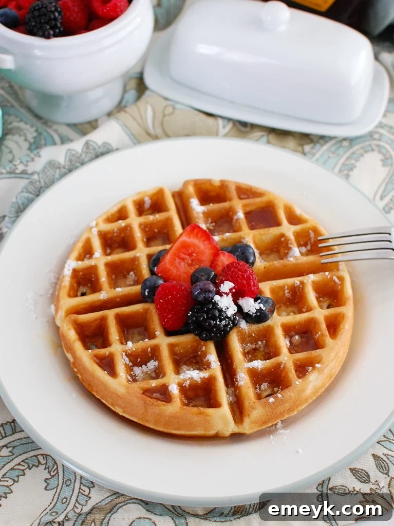 Fluffy Greek Yogurt Waffles 2 Golden brown Greek Yogurt Waffles stacked on a white plate with fresh berries and syrup.