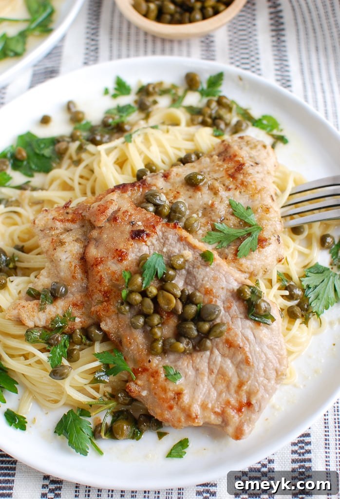 Tender Veal Piccata served on a plate with a fork, garnished with fresh parsley.