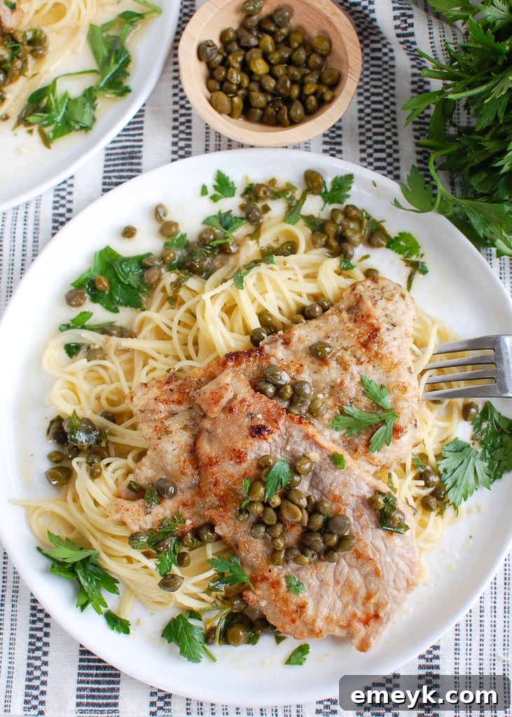 A serving of Veal Piccata on a white plate, showcasing the golden veal and the rich lemon-butter-caper sauce.