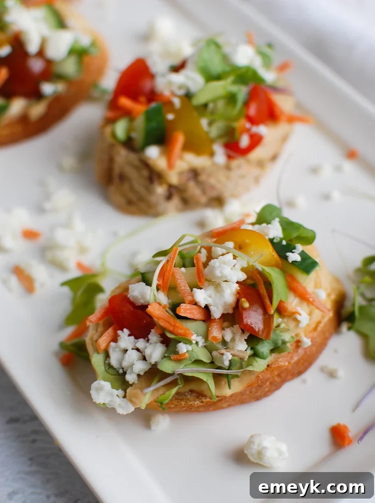 Delicious Mediterranean Crostini with hummus and fresh vegetables on a white plate, garnished with herbs.