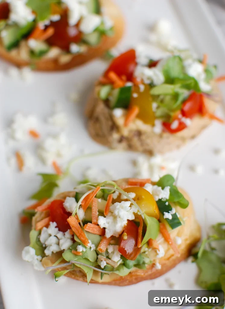 Close-up of Mediterranean Crostini ingredients: fresh vegetables, crumbled feta, and hummus on a white platter.