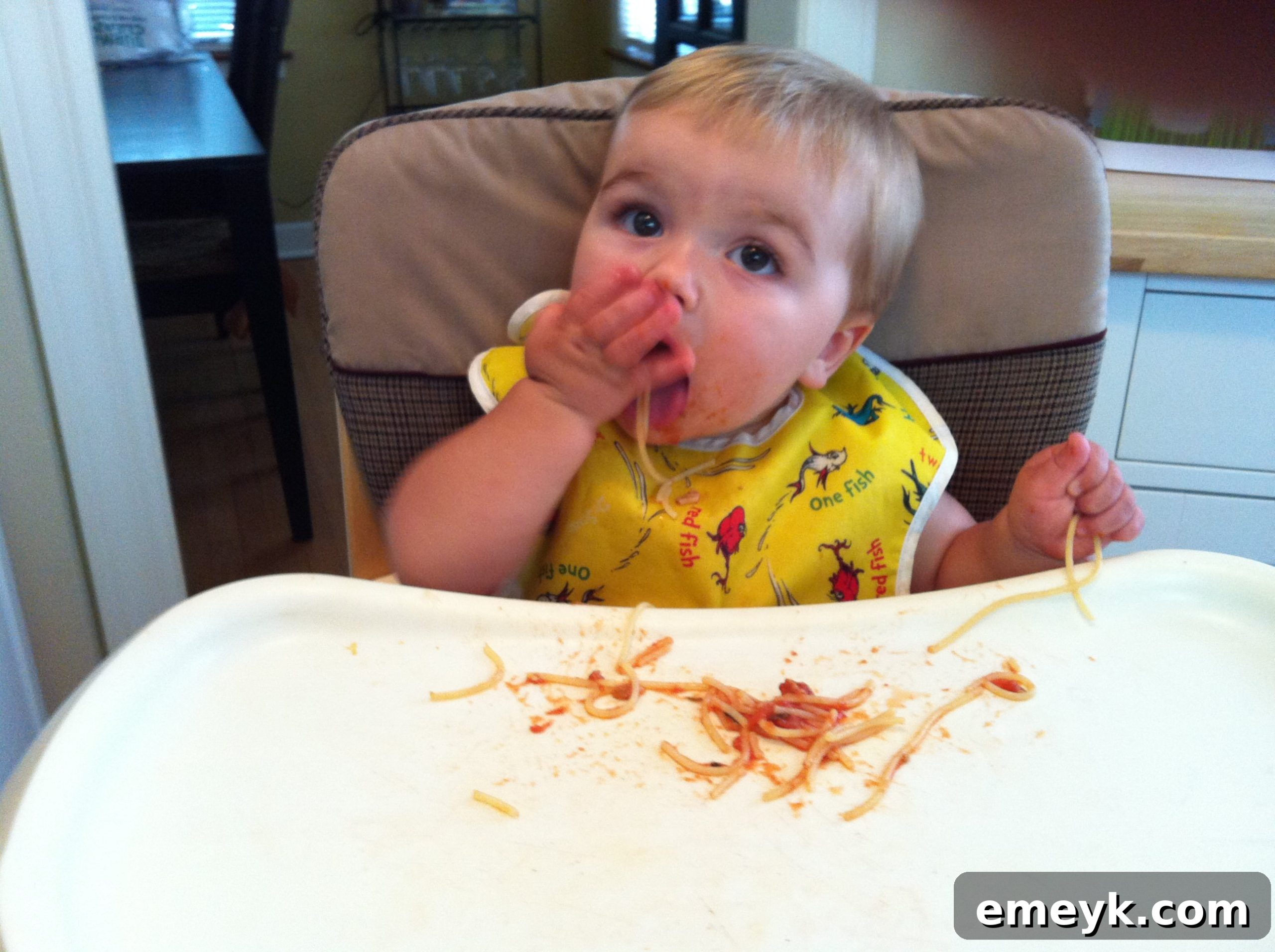 Close-up of a baby's hands covered in spaghetti sauce during a meal