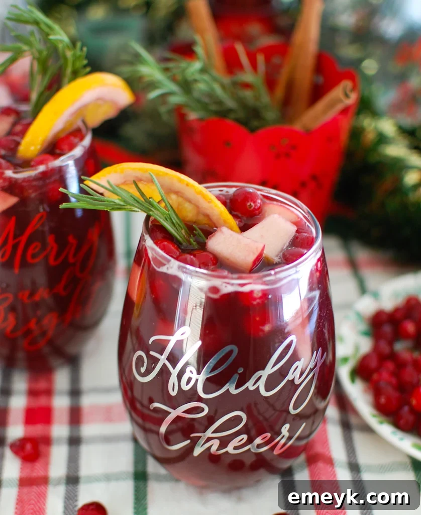 Close-up of a glass of Christmas Sangria with ice, fresh rosemary, and a cinnamon stick garnish