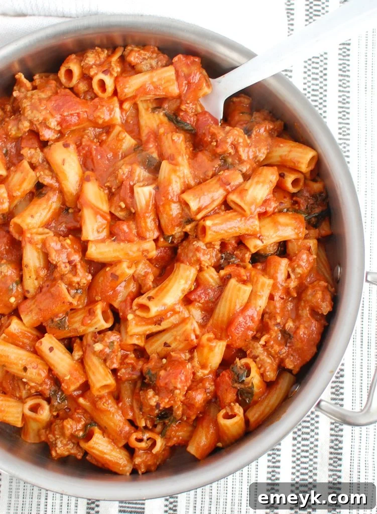 Italian Sausage Pasta ready to be eaten, with a white spoon showing its creamy texture.