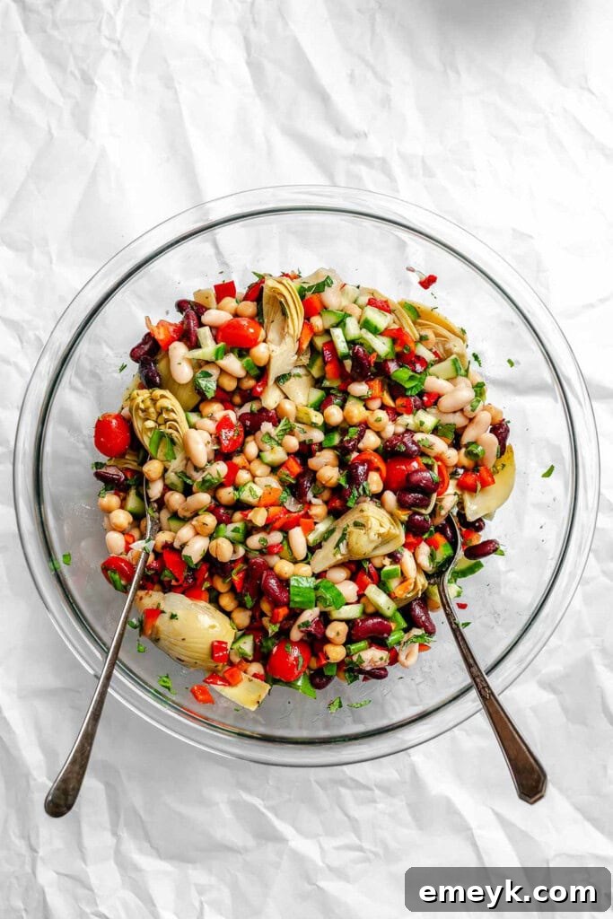 Two spoons tossing the mixed Mediterranean Three Bean Salad ingredients