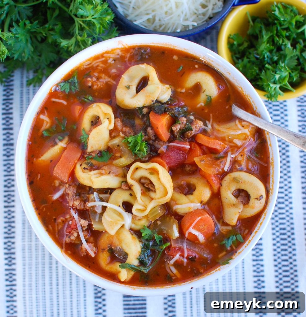 A ladle serving Tortellini Sausage Soup from a pot into a white bowl, showing the comforting steam and rich ingredients.