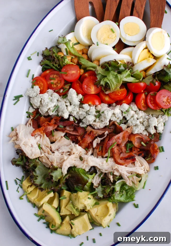 Close-up of a meticulously arranged Cobb Salad featuring eggs, chicken, bacon, avocado, tomatoes, and blue cheese, highlighting its rich textures and colors
