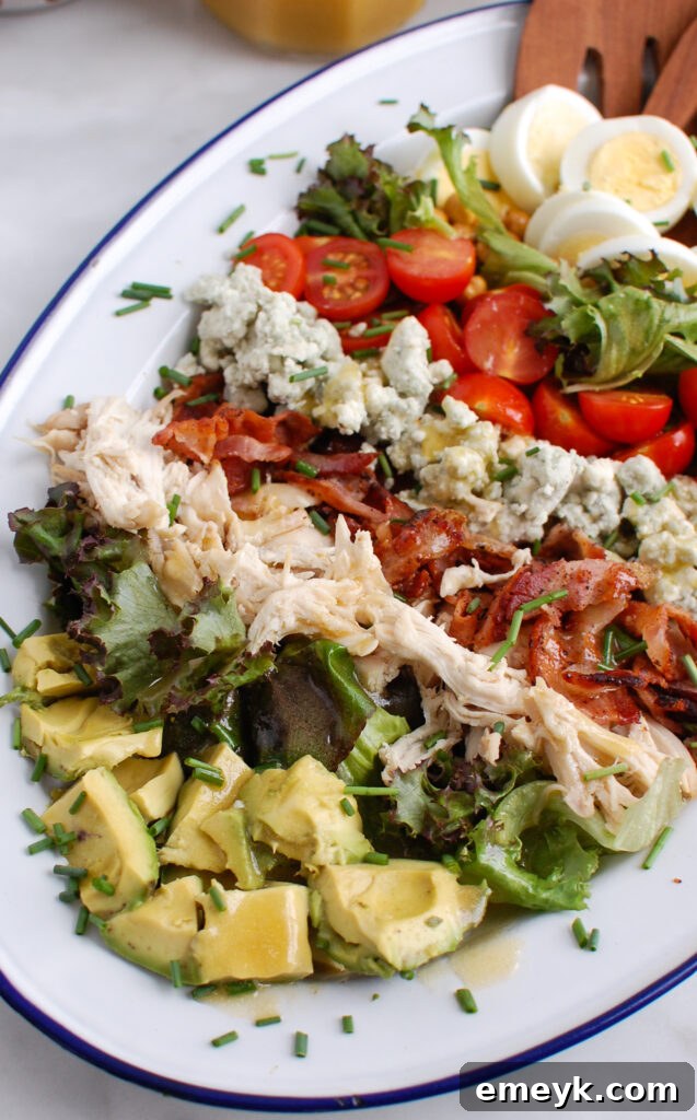 A large serving platter of Cobb Salad with wooden tongs, ready to be served buffet-style