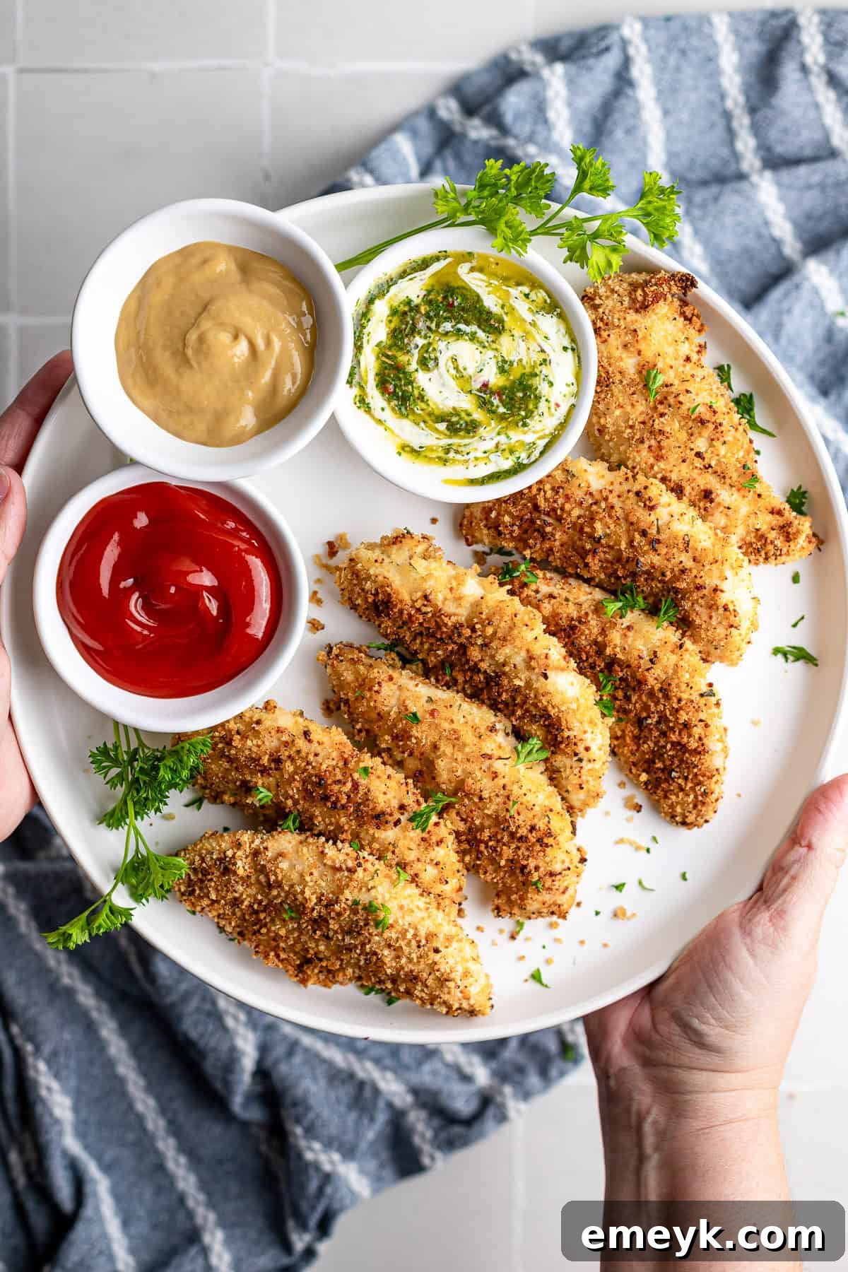Perfectly Crispy Baked Chicken Tenders 2 Crispy baked chicken fingers on a white plate, golden brown and ready to serve with three dipping sauces.