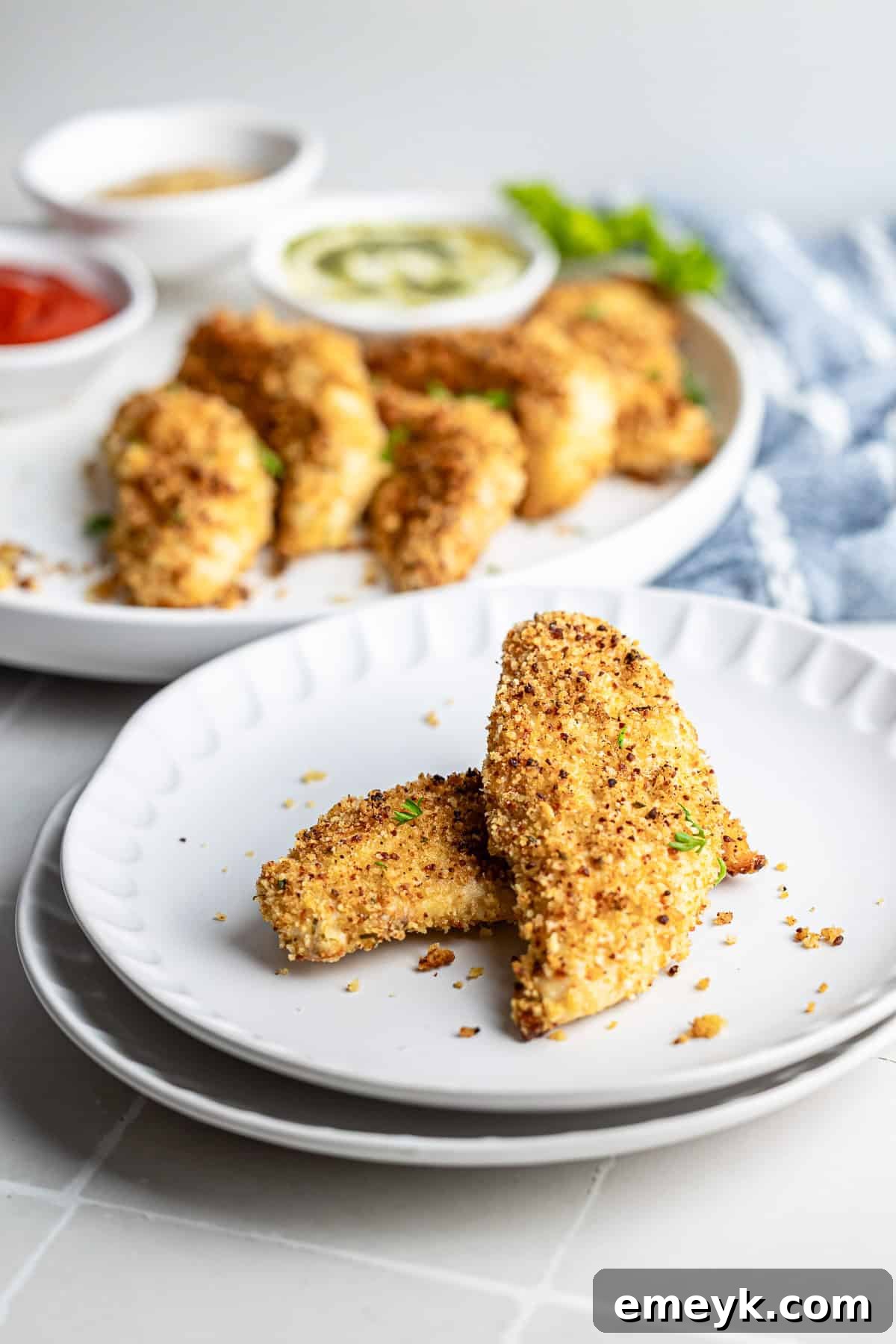 Perfectly Crispy Baked Chicken Tenders 8 Baked chicken tenders plated on a white dish with herbs for garnish.