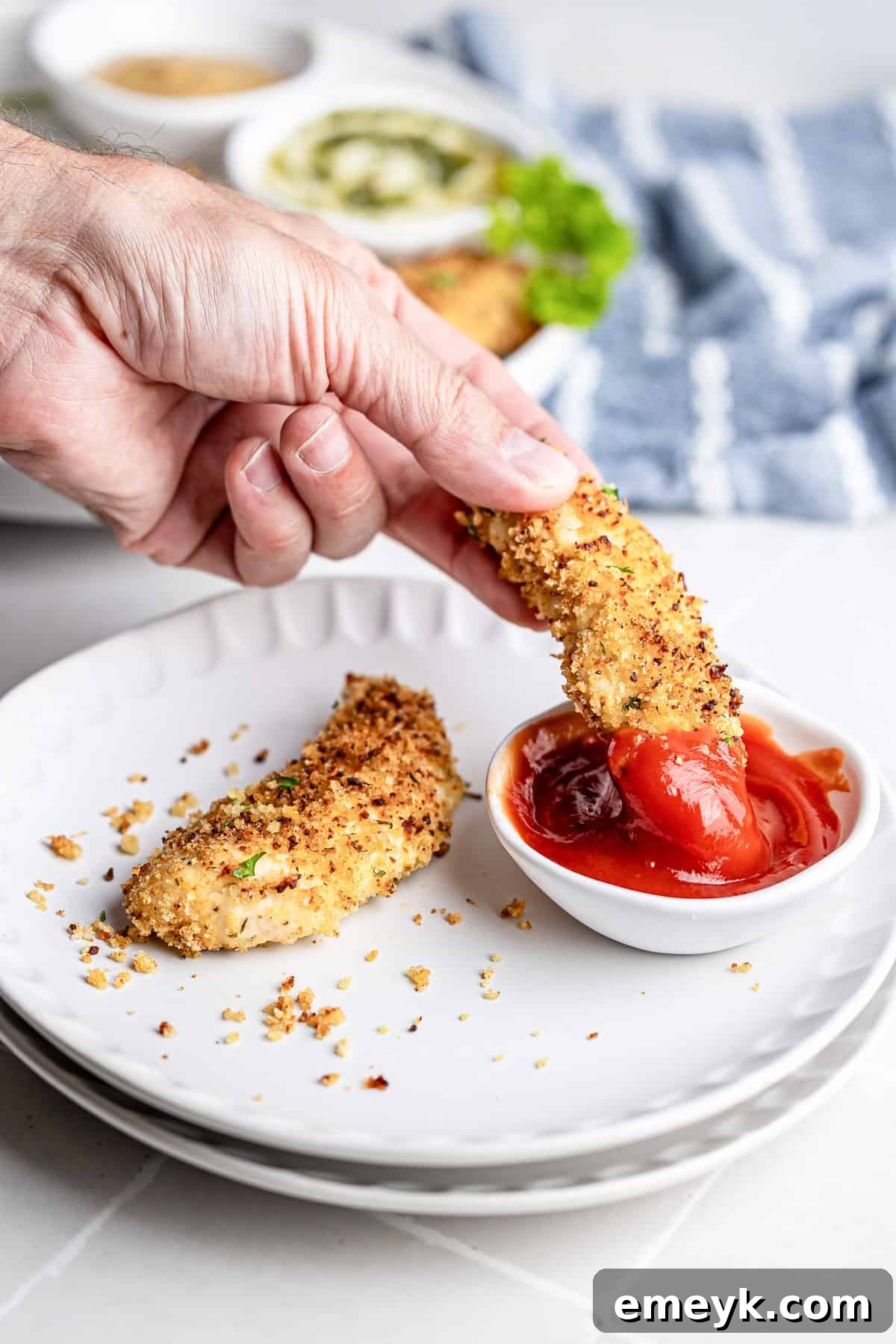 Perfectly Crispy Baked Chicken Tenders 10 Baked chicken tender being dipped into a small bowl of ketchup.