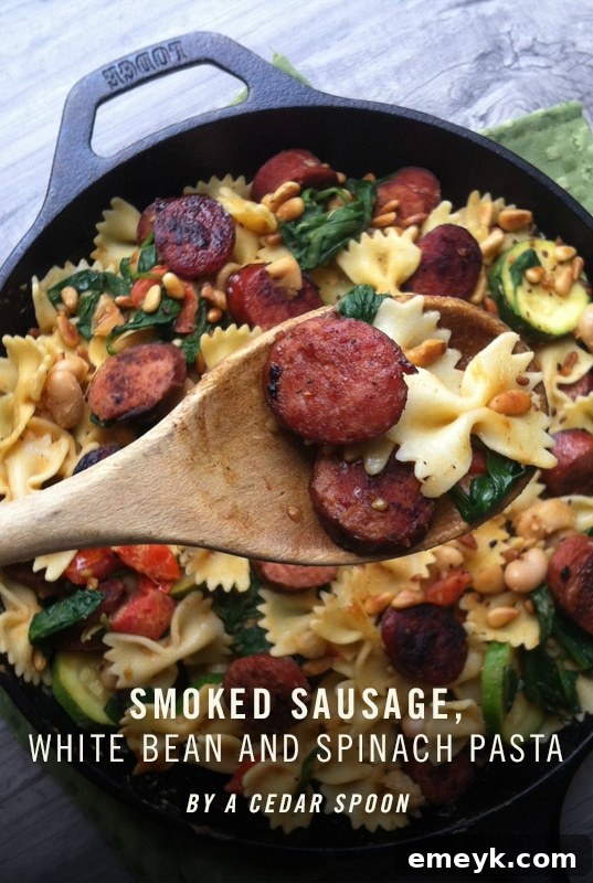 Smoked Sausage Pasta with White Beans, Spinach, and Toasted Pine Nuts in a skillet