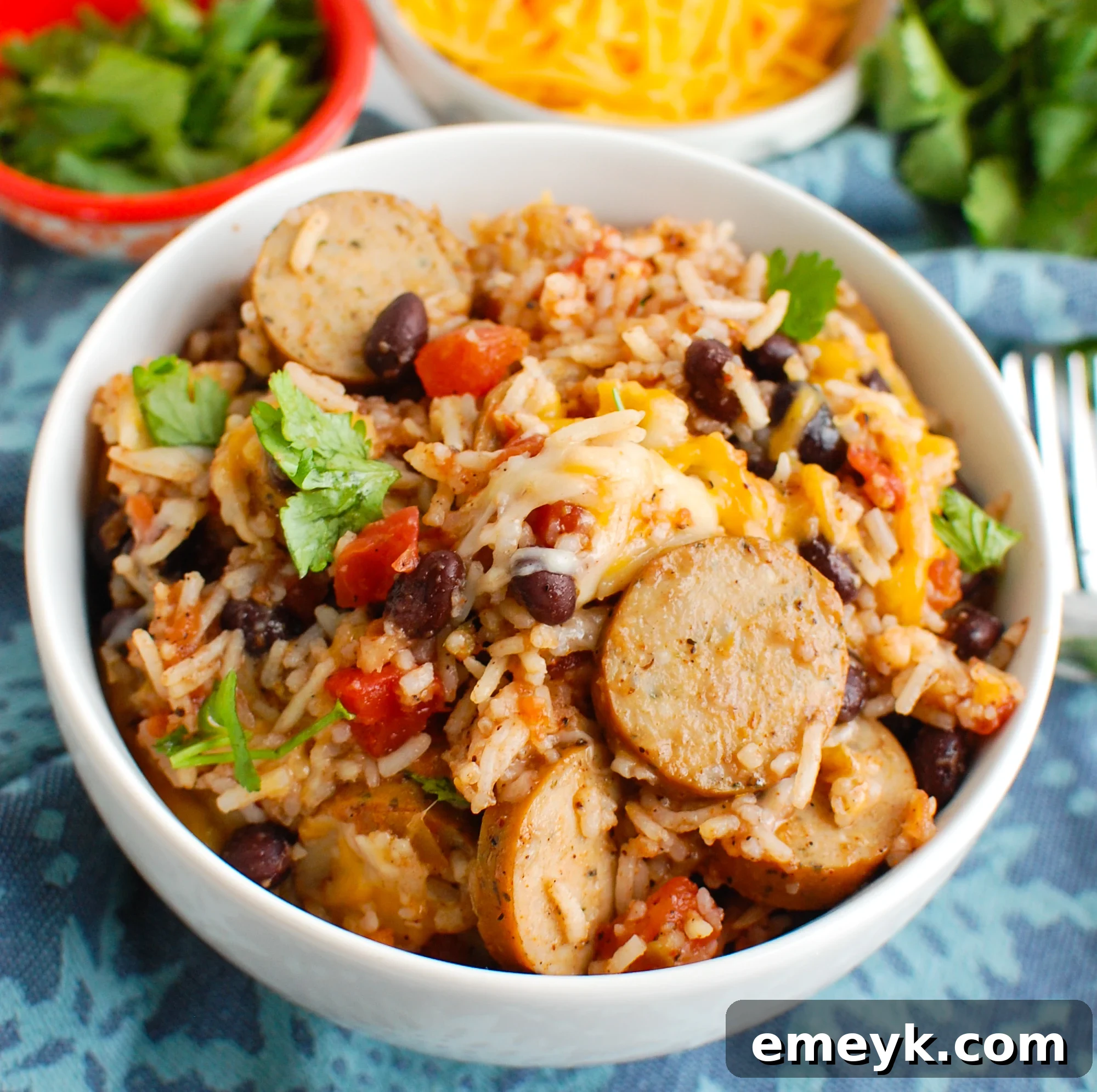 A warm serving of sausage and bean casserole in a white bowl, garnished with fresh herbs.