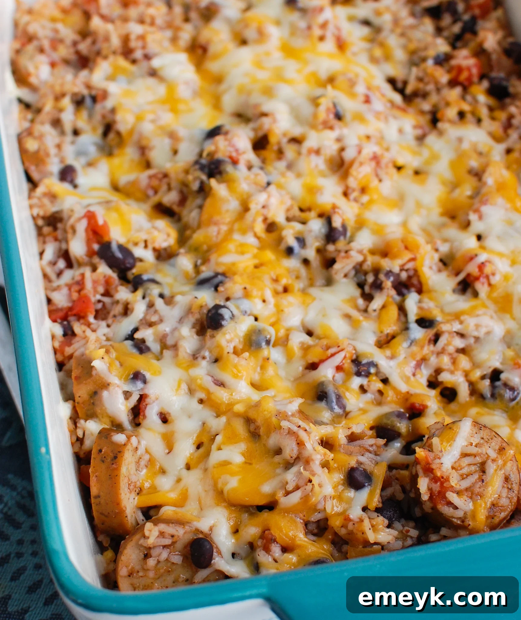 A vibrant sausage and bean casserole in a stylish teal baking dish, fresh from the oven.