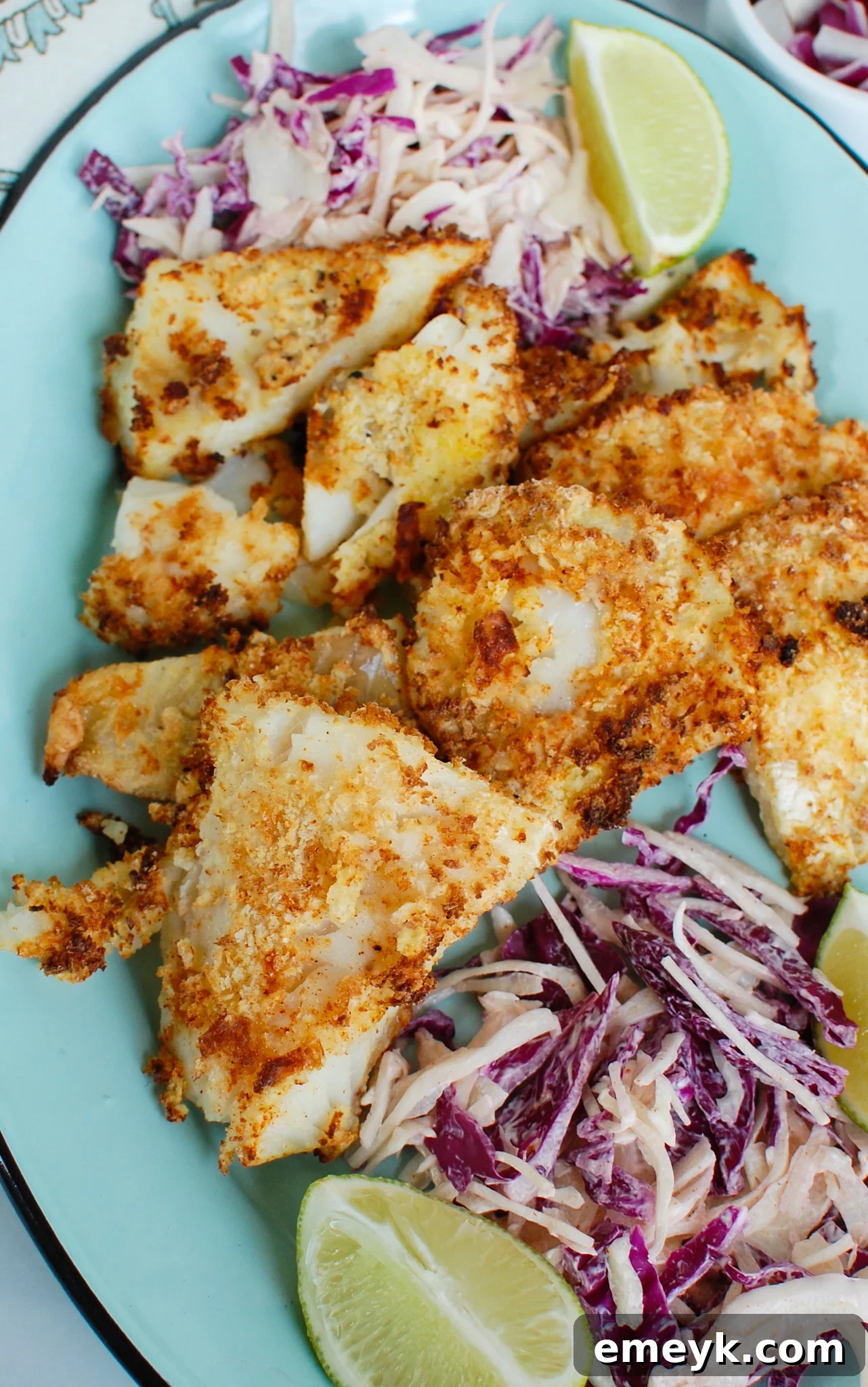 Crispy Air Fryer Cod on a blue plate with lemon wedges and fresh herbs