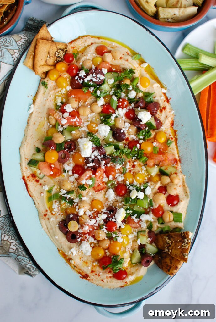 Mediterranean Hummus Board 4 Hummus Platter generously topped with fresh ingredients, served with crispy pita chips and various vegetables for dipping.