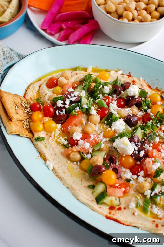Mediterranean Hummus Board 5 Hummus Platter beautifully arranged on a teal serving dish, garnished with fresh toppings and ready to be enjoyed.
