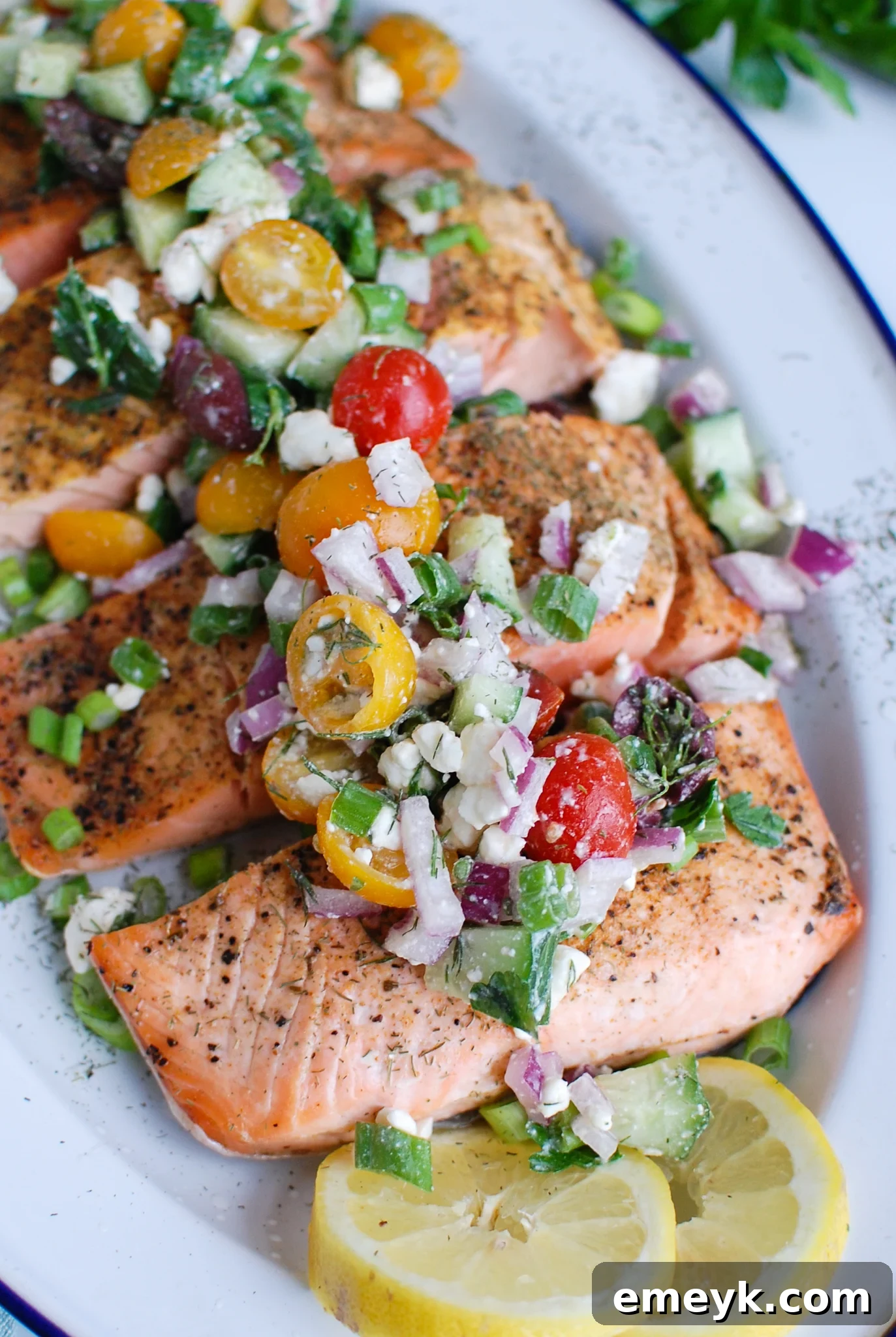 Sundrenched Mediterranean Salmon Bake 2 Perfectly cooked Mediterranean Salmon fillets adorned with a colorful Greek topping including fresh tomatoes, cucumbers, olives, and feta cheese.