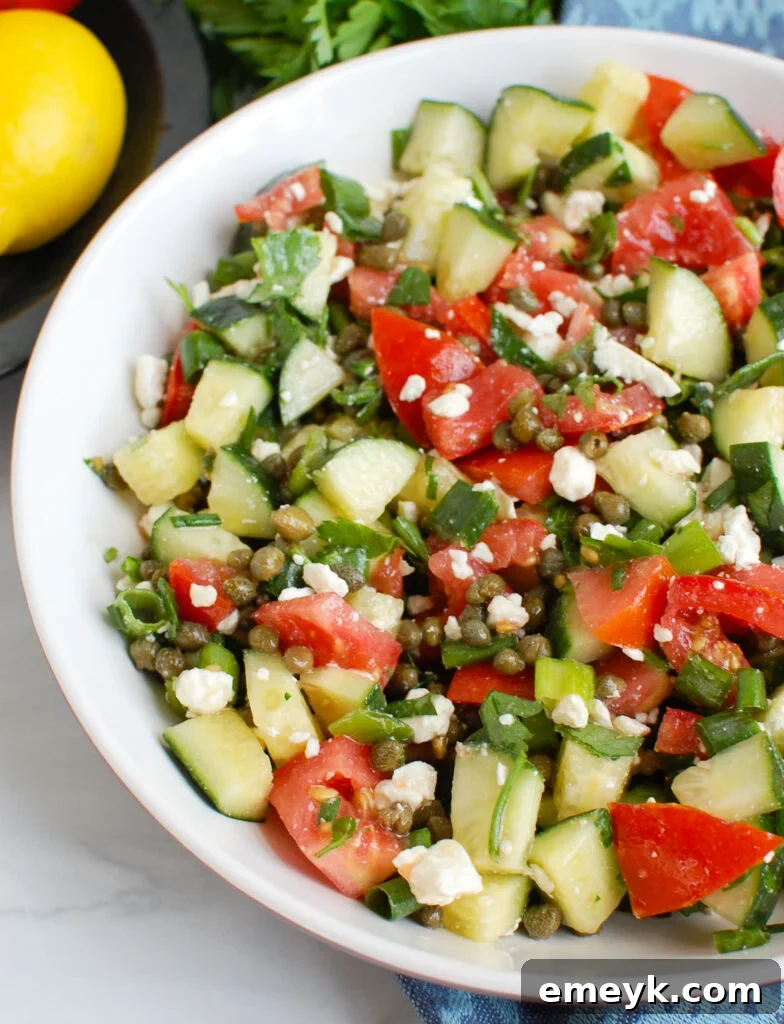 Large white bowl filled with Tomato and Cucumber Salad with Capers, garnished with fresh herbs