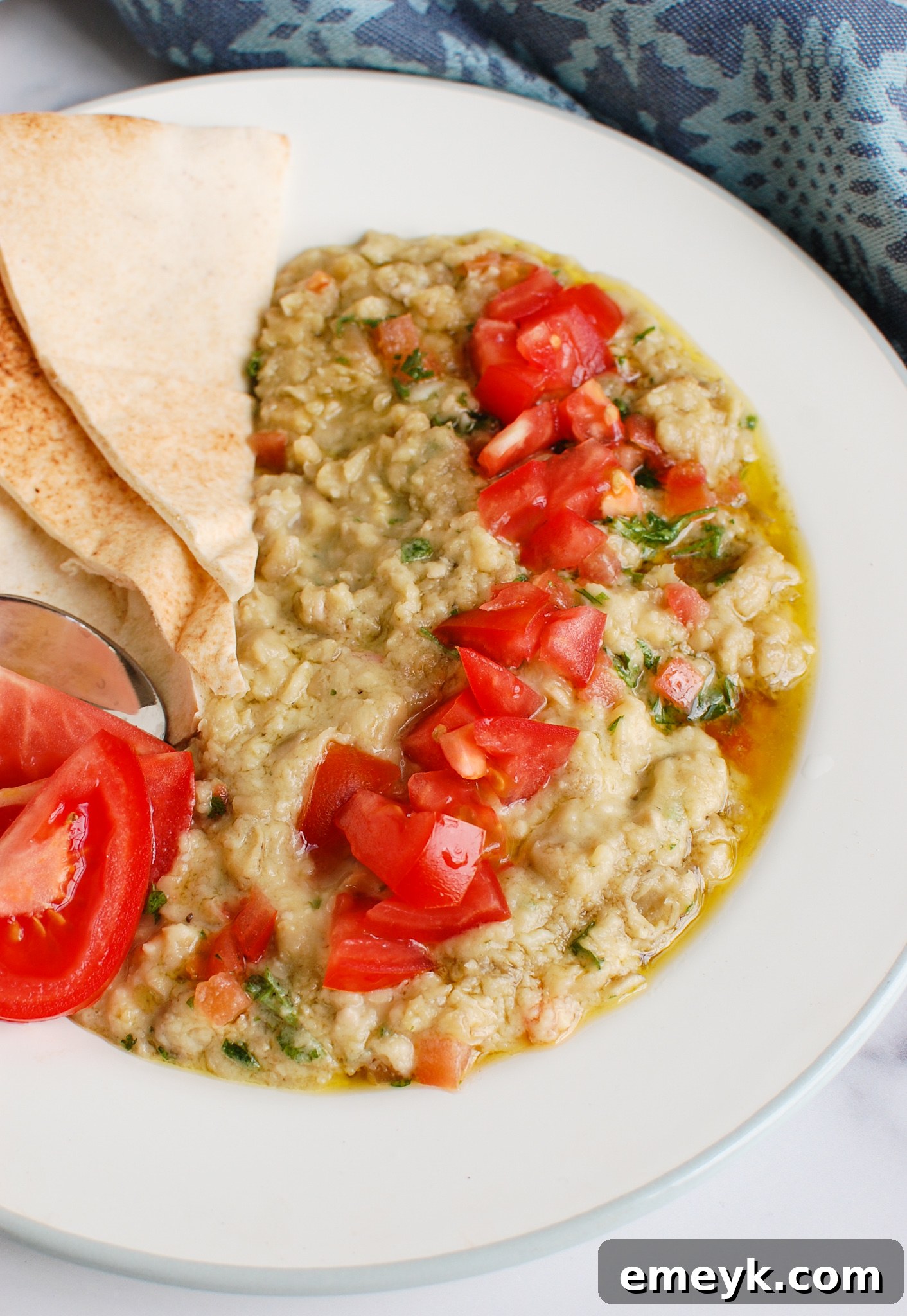 Ful Medames served warm on a white plate, garnished with fresh herbs and tomatoes.