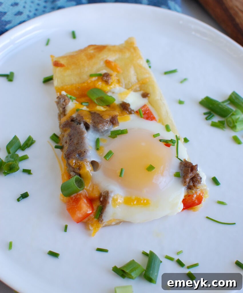 A perfectly cooked slice of Turkey Sausage and Egg Puff Pastry Pizza resting on a crisp white plate, showcasing its flaky crust and rich toppings.