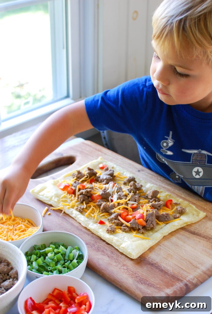 A child's hands carefully arranging toppings, including sausage and cheese, on a puff pastry pizza, highlighting a family-friendly cooking activity.