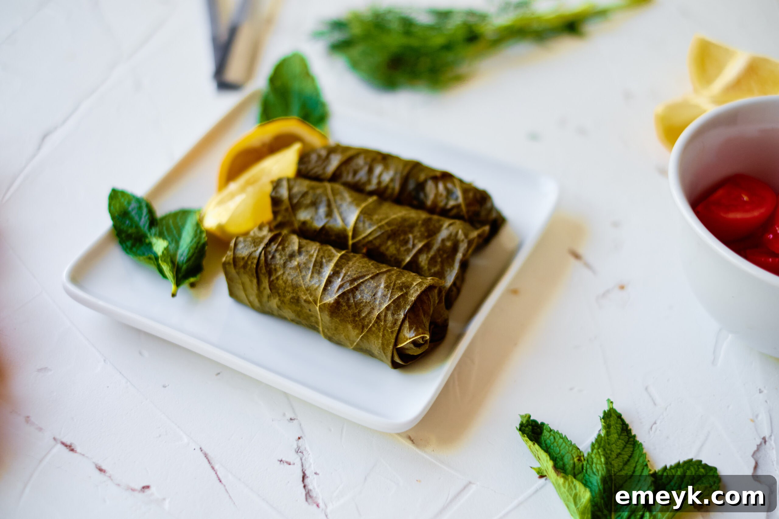 Effortless Homemade Dolma 3 Fresh ingredients for making stuffed grape leaves, including rice, pine nuts, fresh mint, dill, and a jar of grape leaves, arranged on a rustic wooden board.