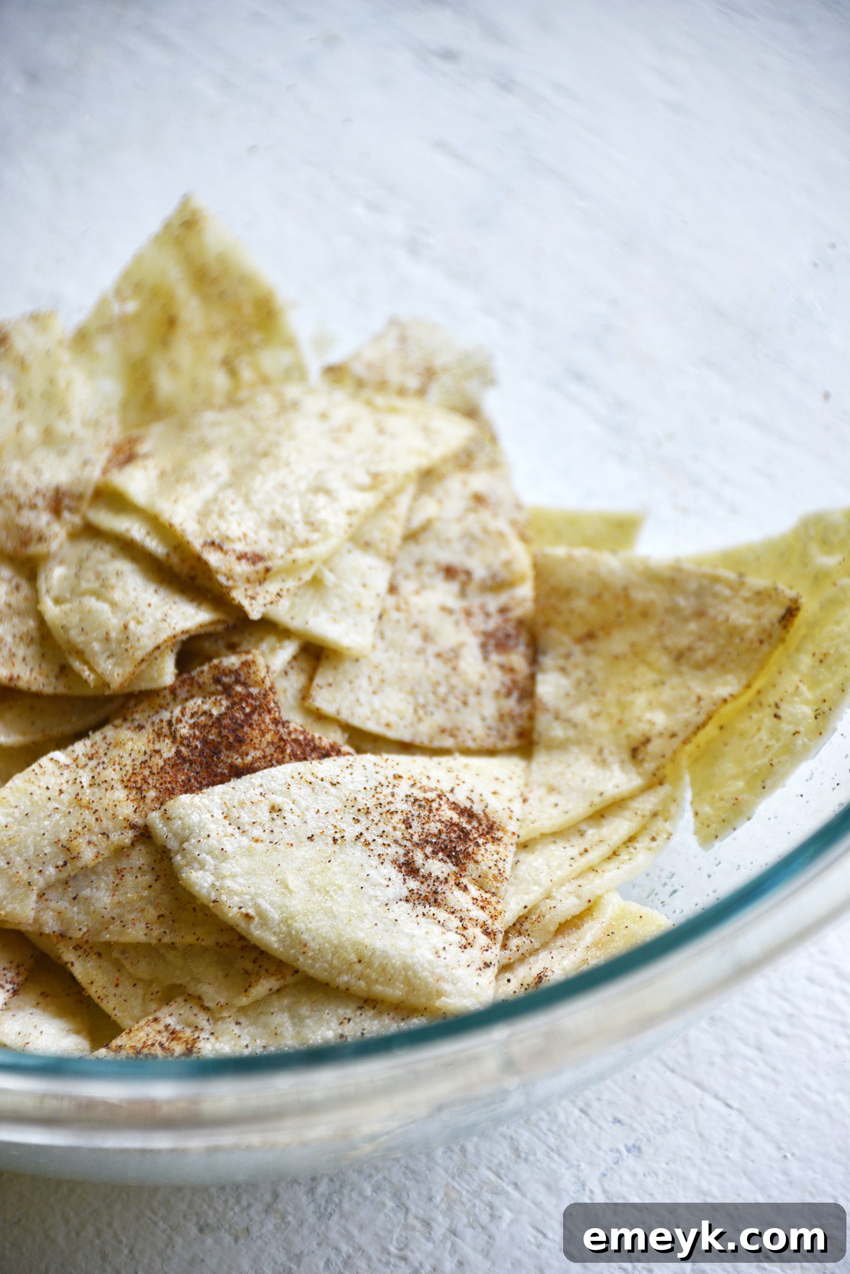 Tortilla wedges being gently tossed in a large bowl with oil and a blend of savory spices.