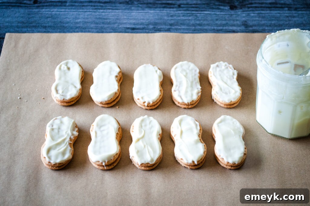 A hand dipping a Nutter Butter cookie into melted white chocolate, demonstrating the dipping process for Mummy Cookies.
