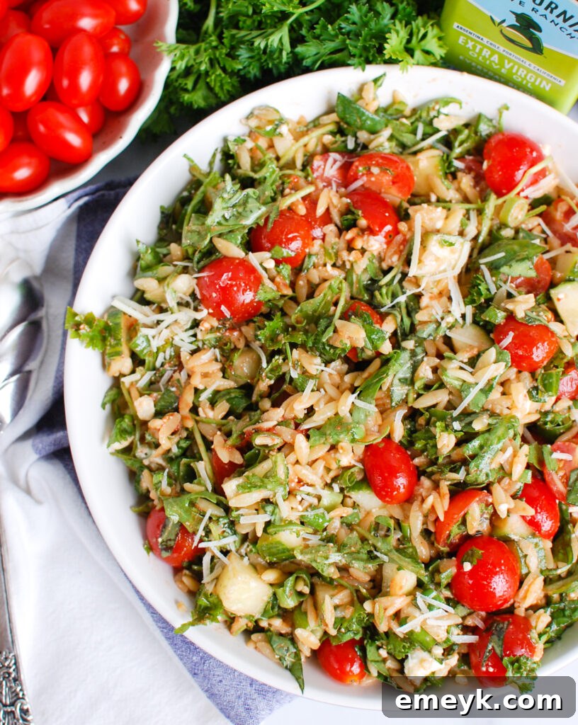A large bowl of vibrant Tomato Feta Orzo Salad, brimming with halved cherry tomatoes, crumbled white feta cheese, and green herbs.