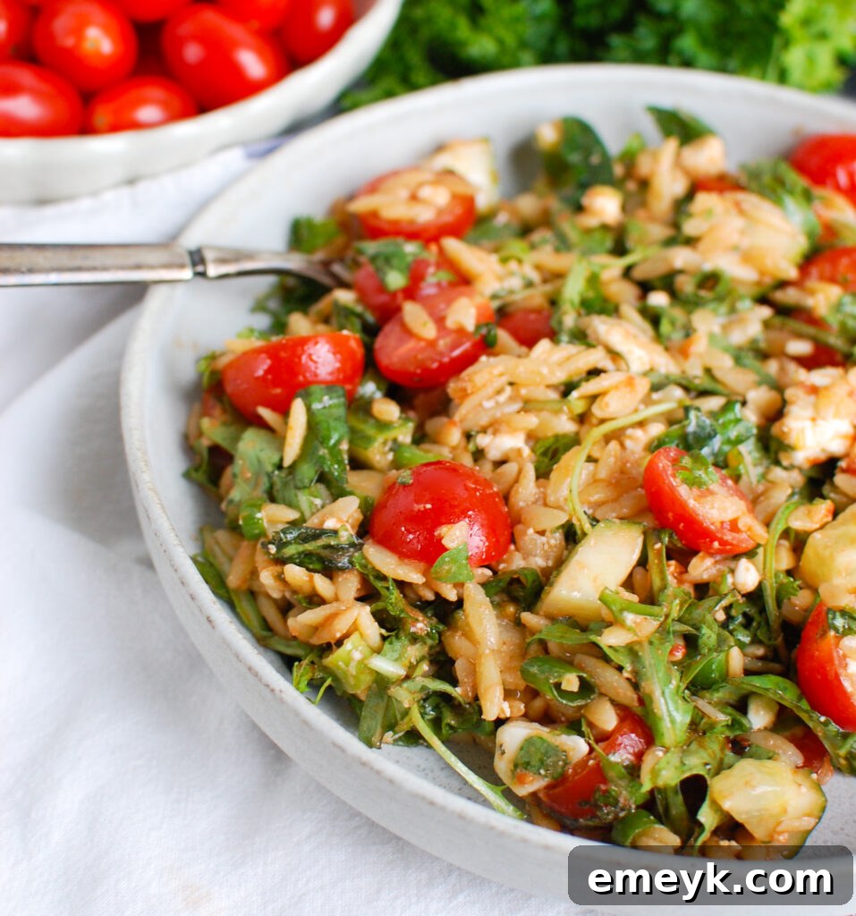 Close-up of Tomato Feta Orzo Salad in a rustic bowl, with a fork poised to scoop, highlighting the textures of orzo, feta, and fresh herbs.