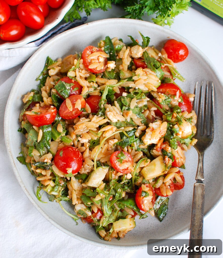 A close-up, inviting shot of Tomato Feta Orzo Salad with a fork, emphasizing its delightful freshness and a hint of the creamy feta.