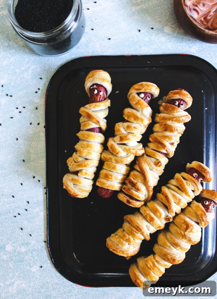 Pharaoh Franks 2 Mummy Hot Dogs arranged on a black plate, showcasing their golden-brown puff pastry 'bandages' and cute eyes.
