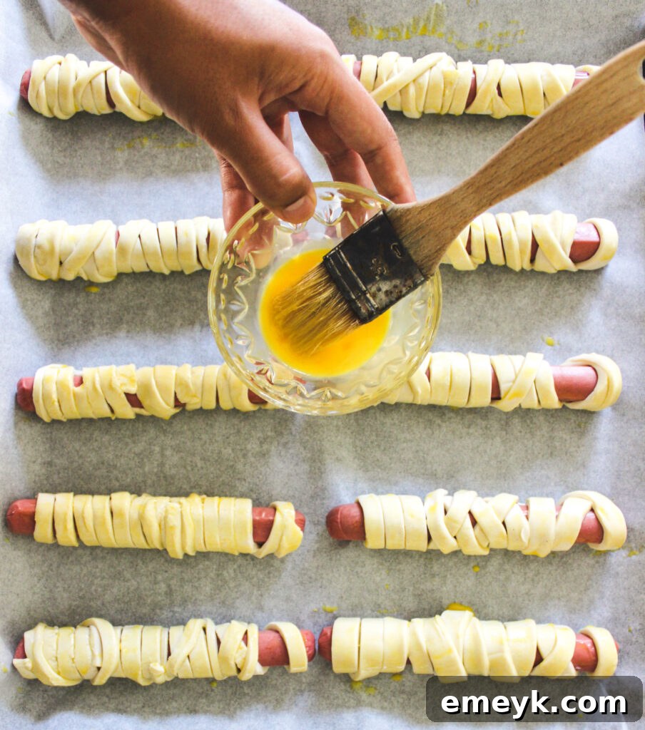 Pharaoh Franks 6 Mummy Hot Dogs on a baking sheet, brushed with egg wash and ready to be baked to a golden perfection.