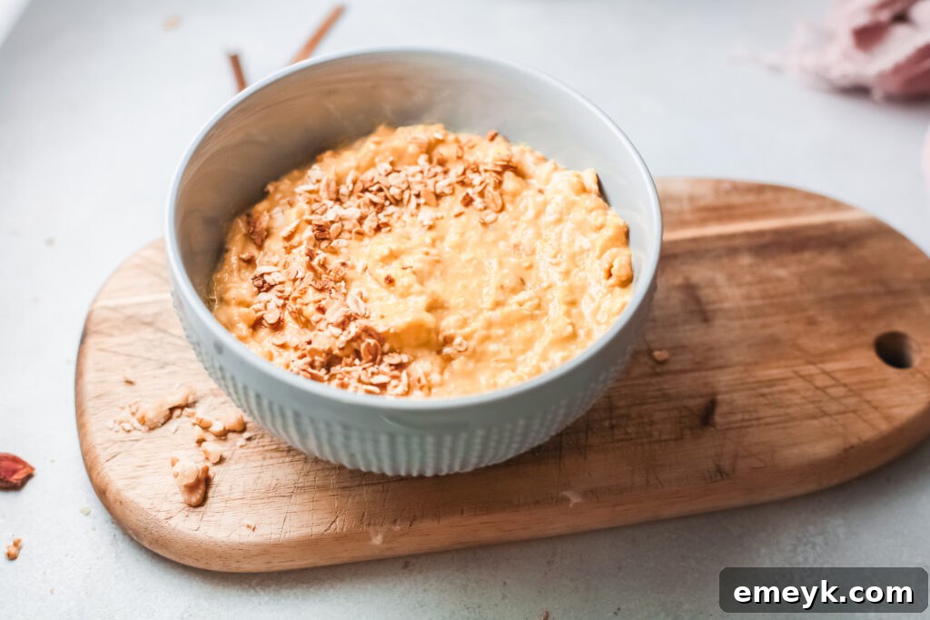 Close-up of a bowl of Easy Pumpkin Oatmeal garnished with fresh banana slices and a sprinkle of pumpkin pie spice on a wooden background.