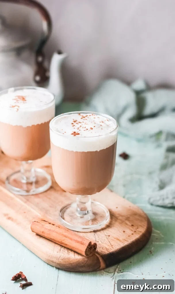 Instant Pot Spiced Chai Latte 2 Instant Pot Chai Tea Latte served in a glass mug, with steam rising, on a rustic wooden board, garnished with a cinnamon stick.