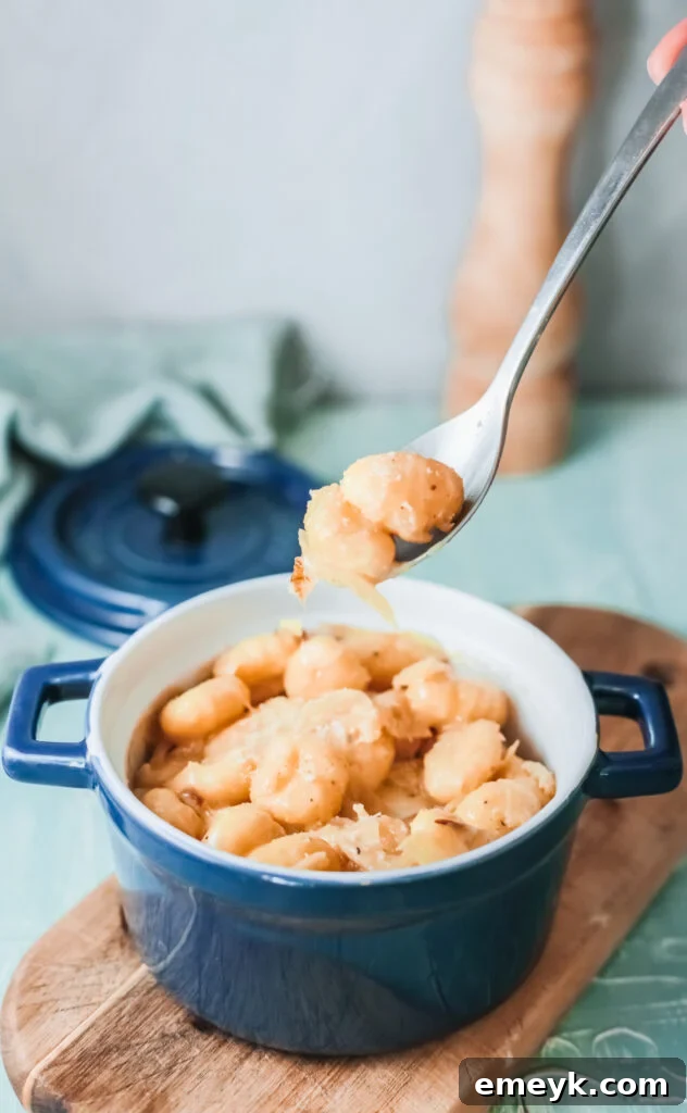 A close-up shot of One Pot French Onion Gnocchi in a blue bowl with a fork, showing melted cheese and golden onions.