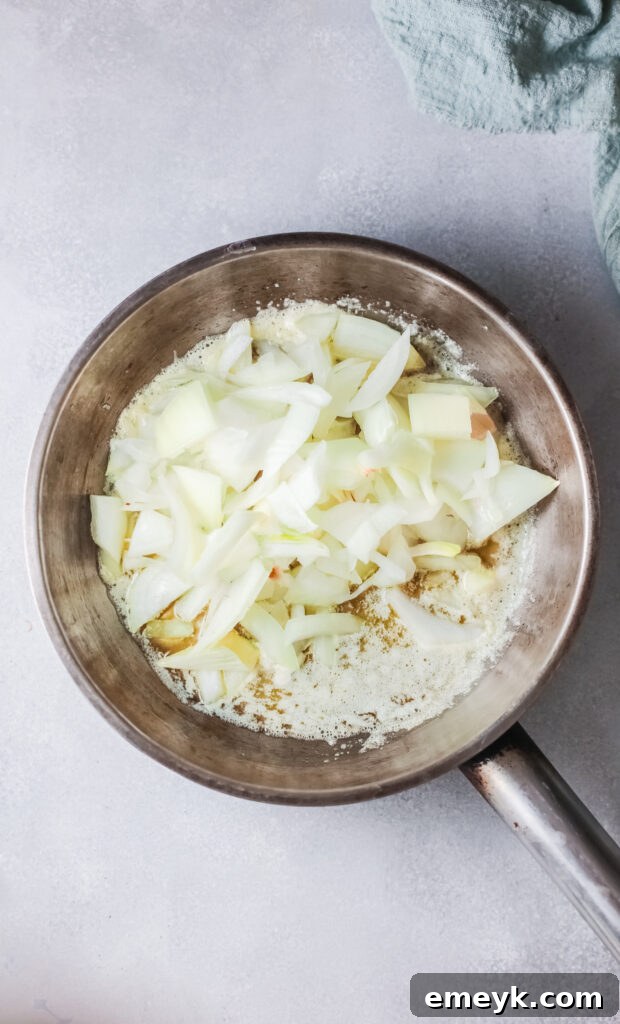 Thinly sliced onions sizzling and caramelizing in butter in a pan, turning golden brown.