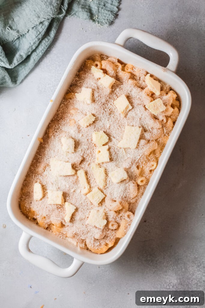 Pumpkin Mac and Cheese topped with breadcrumbs, diced butter, and Parmesan cheese, ready for baking.