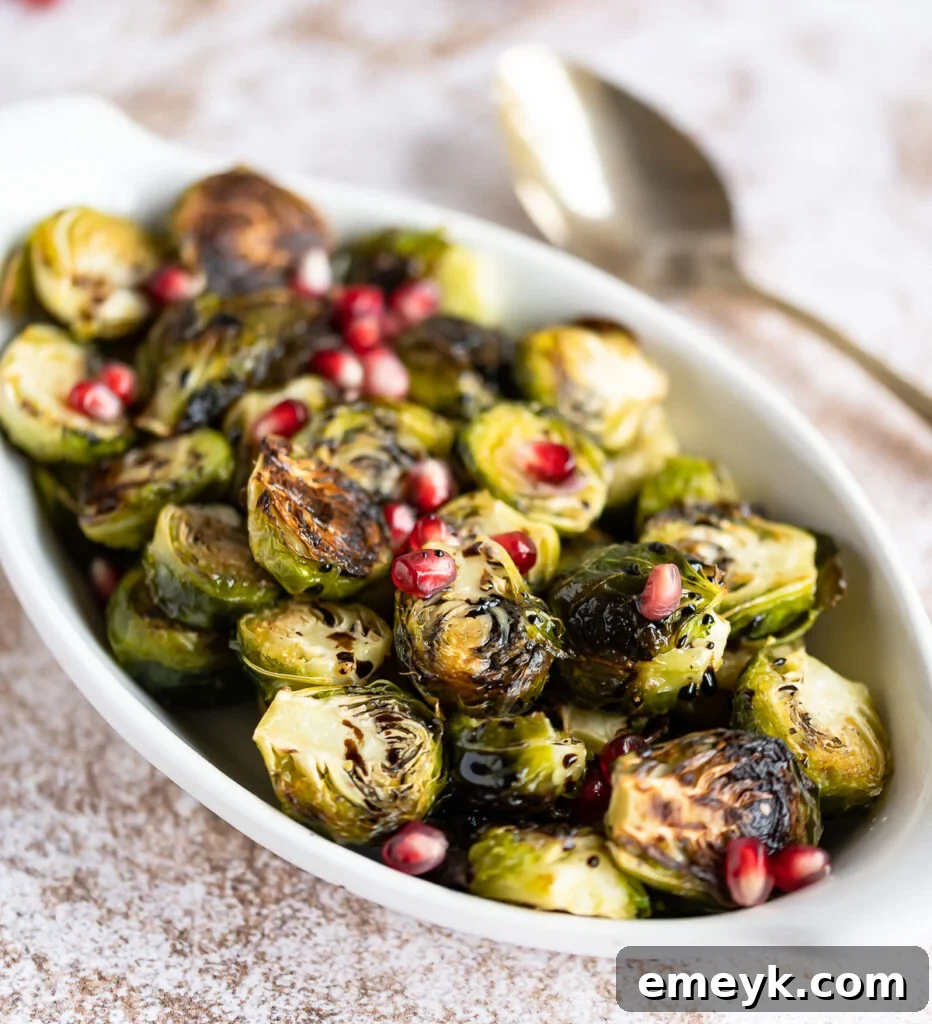 Beautifully plated Roasted Balsamic Brussels Sprouts in a white dish, garnished with vibrant pomegranate arils, ready to serve.
