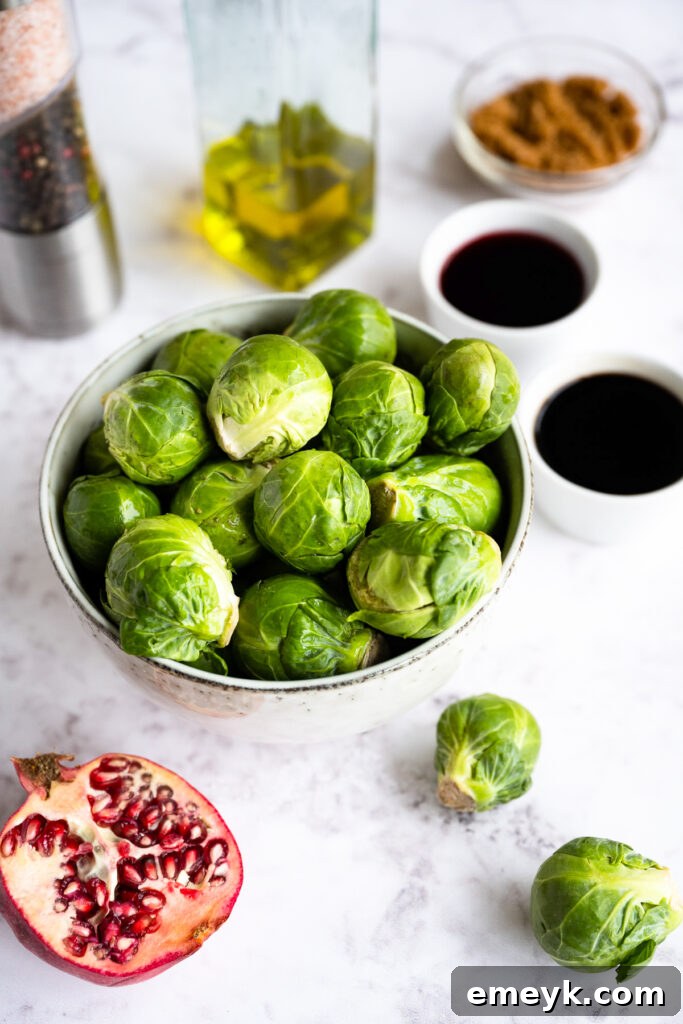 Fresh Brussels sprouts, olive oil, balsamic vinegar, pomegranate juice, and brown sugar laid out on a wooden surface, showcasing the key ingredients for the recipe.