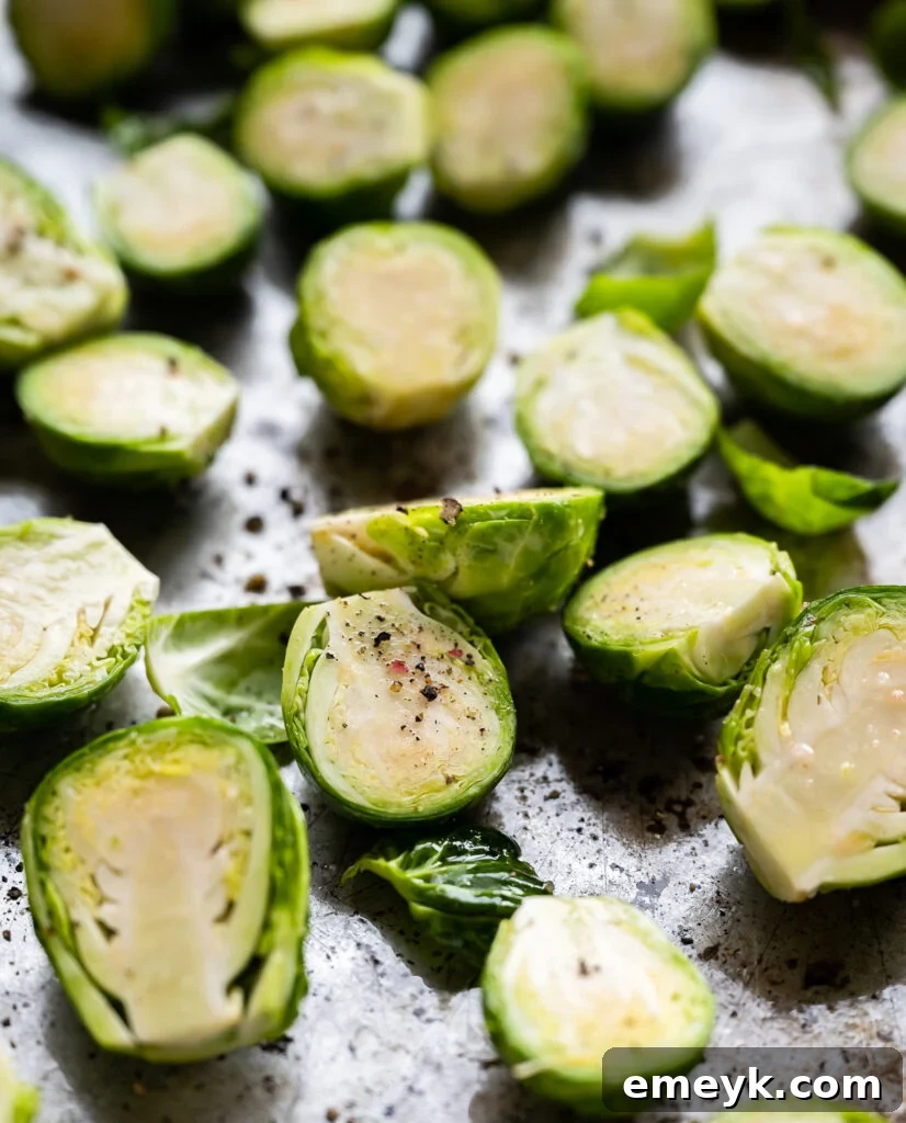 Brussels sprouts coated in olive oil, spread in a single layer on a baking sheet, seasoned with salt and pepper, ready for roasting.